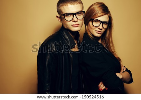 Portrait of gorgeous red-haired fashion twins in black clothes wearing trendy glasses and posing over beige background together. Perfect hair. Natural make-up. Perfect skin. Studio shot