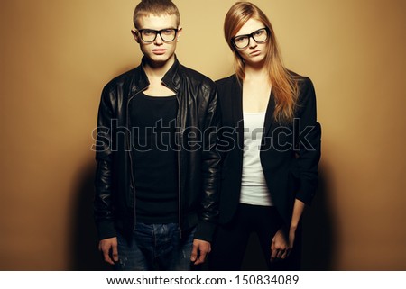 Portrait of gorgeous red-haired fashion twins in black clothes wearing trendy glasses and posing over beige background together. Perfect hair. Natural make-up. Perfect skin. Studio shot