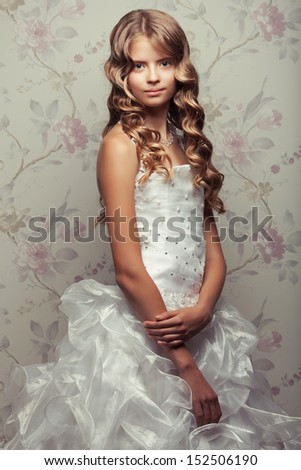 Portrait of a little princess in white vapory classic dress with pearls posing over vintage background. Perfect glossy long hair. Retro & Vogue style. Studio shot