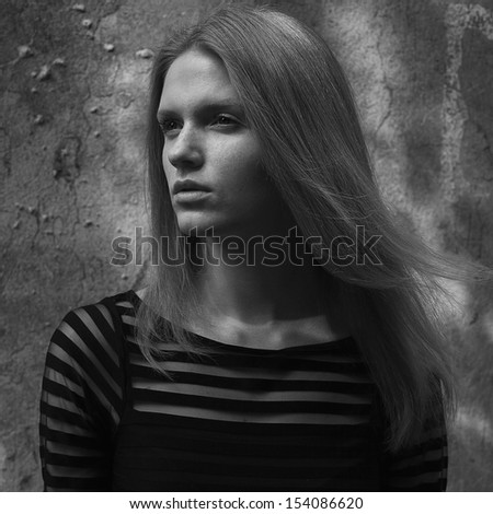 Portrait of a beautiful model with freckles on her face posing in a black cocktail dress over old house\' wall. Healthy long hair. Daylight. Vogue style. Black & white (monochrome) outdoor shot