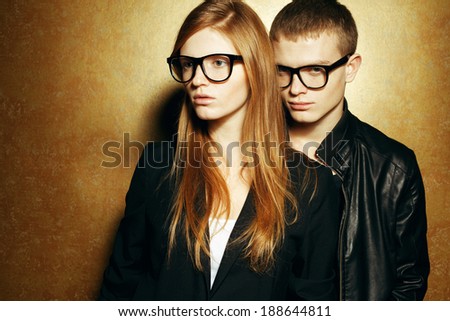 Eyewear concept. Portrait of gorgeous red-haired twins in black clothes wearing trendy glasses and posing over golden background together. Perfect hair & skin. Hipster style. Copy-space. Studio shot
