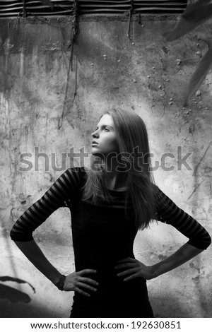 Arty portrait of a beautiful model in black striped cocktail dress with jabot of tree\'s leaves posing over old stone wall with metal constructions. Urban (vogue) style. Black and white outdoor shot