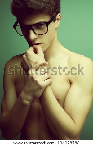 Male beauty, eyewear concept. Emotive portrait of handsome muscular male model with nice body in trendy glasses posing over green background.Perfect skin and body. Studio shot