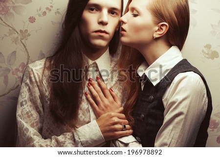 Gothic hipsters concept. Portrait of beautiful long haired people in vintage style: handsome guy with brown hair & whispering to his ear gorgeous red-haired girl posing together. Close up. Studio shot