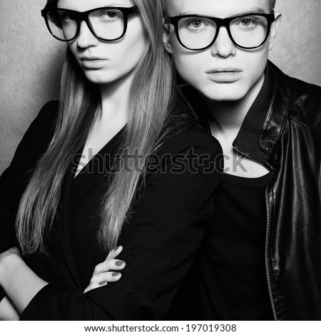 Eyewear concept. Portrait of gorgeous fashion twins in black clothes wearing trendy glasses and posing over metal background together. Perfect hair and skin. Natural make-up. Studio shot