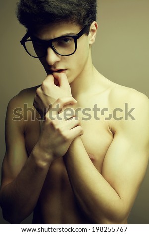 Male beauty, eyewear concept. Emotive portrait of handsome muscular male model with nice body in trendy glasses posing over gray background. Vogue style. Perfect skin and body. Studio shot