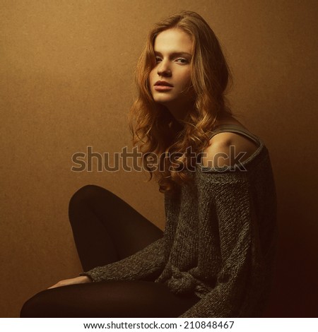 Emotive portrait of fashionable model with long curly red hair and natural make-up posing over wooden background. Perfect skin. Urban grunge style. Studio shot