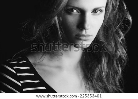 Emotive portrait of fashionable model with curly hair and natural make-up posing over black background. Perfect skin. Retro style. Black and white (monochrome) studio shot