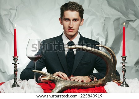 Baroque dinner of blue blood aristocrat. Handsome man eating fresh meat at vintage restaurant. Baroque accessories: deer horn, red & white table sheet. Expensive watch. Retro style. Indoor shot