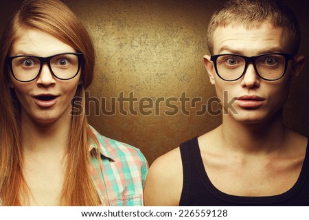Eyewear concept. Portrait of gorgeous red-haired twins in casual shirts wearing trendy glasses and posing over golden background together with wow faces (duck-face). Hipster style. Studio shot