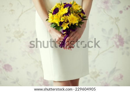 Bride\'s hands with wedding bouquet of violet and yellow flowers over stylish white dress. Vintage style. Close up. Copy-space. Indoor shot