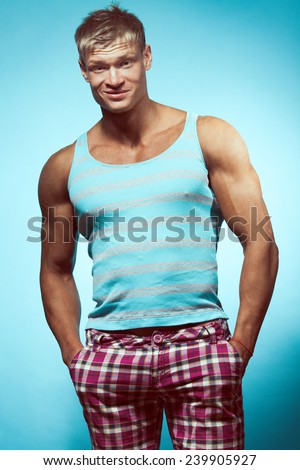 Male beauty & fashion concept. Portrait of funny handsome muscular male model in trendy summer clothing posing over blue background. Blond hair and healthy clean skin. Studio shot