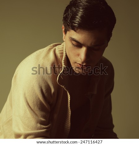 Male beauty concept. Portrait of fashionable young man with stylish haircut wearing trendy cardigan & posing over mustard background. Perfect hair & skin. Hipster style. Close up. Studio shot