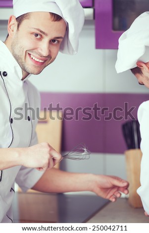 Portrait of a smiling male chef with his coworker cooking food and standing in the modern kitchen of restaurant. Indoor shot