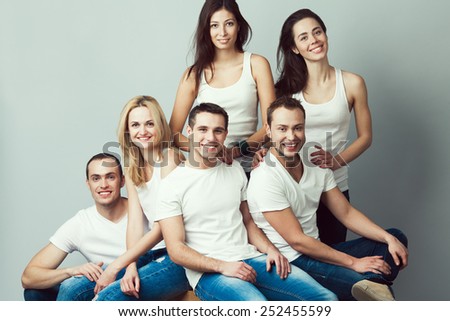 Happy together concept. Group portrait of healthy boys & girls in white t-shirts, sleeveless shirts and blue jeans standing, sitting, posing over gray background. Urban street style. Studio shot
