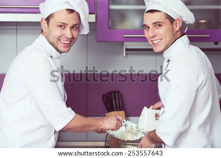 Dessert cooking concept. Portrait of smiling male chefs cooking food and standing in the modern kitchen of restaurant. Indoor shot
