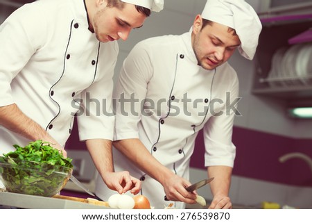 Cooking process concept. Portrait of two funny working men in cook uniform making food in modern kitchen. Indoor shot