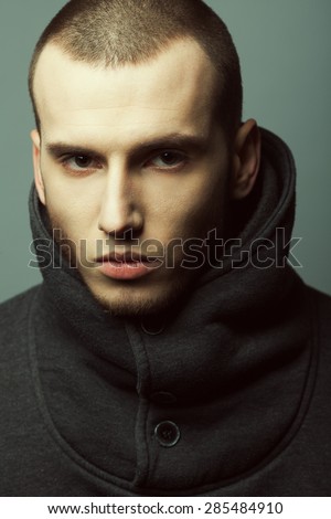 Male beauty concept. Portrait of brutal young man with short hair wearing gray coat with high collar and posing over gray background. Modern street style. Close up. Studio shot