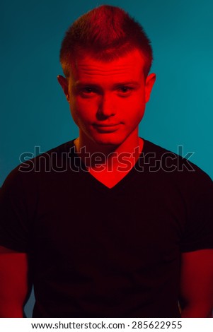 Pop-art style concept. Portrait of smiling young man with short hair wearing black t-shirt and posing over blue background. Hipster style. Close up. Studio shot