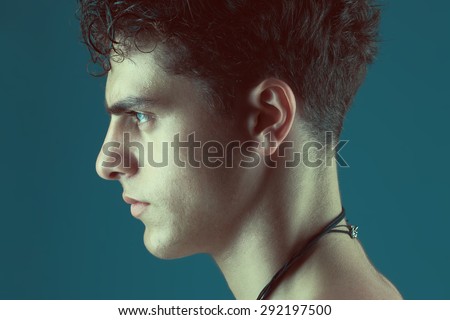 Male beauty concept. Profile portrait of handsome male model posing over blue background. Perfect glossy wet curly hair and healthy clean skin. Close up. Studio shot