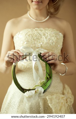 Great event, arty wedding bouquet concept. Bride holding circle made of leaves & orchid blossom and buds over wooden background. Luxurious accessories. Pastel colors. Hipster retro style. Indoor shot