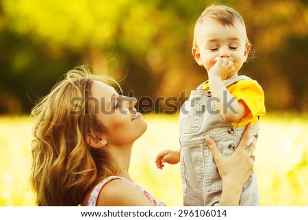 Happy family, friends forever concept. Smiling mother and little son playing together in a park. Mum holding shy baby. Sunny windy summer day. Close up. Copy-space. Outdoor shot