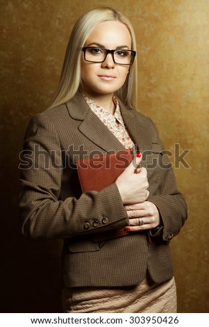 Tough business lady concept. Portrait of elegantly dressed young gorgeous blonde woman in trendy eyewear holding leather notebook. Smart casual style. Studio shot