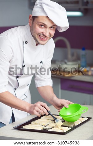 Vegetarian cooking concept. Portrait handsome smiling kitchener in cook uniform making french snack in modern kitchen of restaurant, cafe. Indoor shot