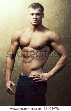 Bodybuilding and body sculpture concept. Beautiful (handsome) muscular male model with perfect body posing over golden background. Studio shot