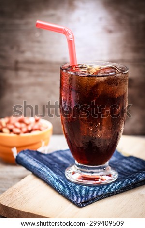 glass of cola with ice and salt roasted peanuts have lighting behind  on wood table and wall
