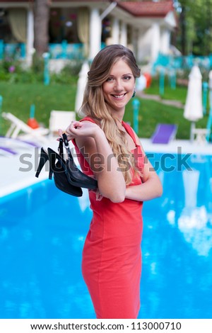 beautiful slim woman in red dress holding her high-heeled sandals
