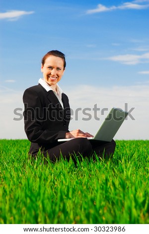 smiley woman with computer sitting at the green meadow