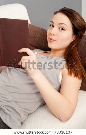 smiley young woman with book lying on sofa
