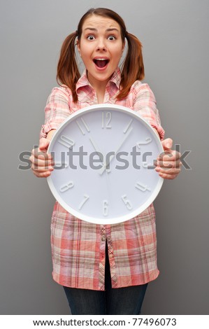 scared young woman showing wall clock over grey background