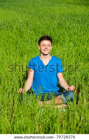 portrait of healthy young man meditation on green grass