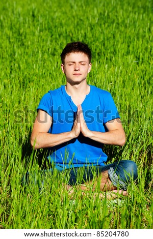portrait of healthy young man meditation on green grass