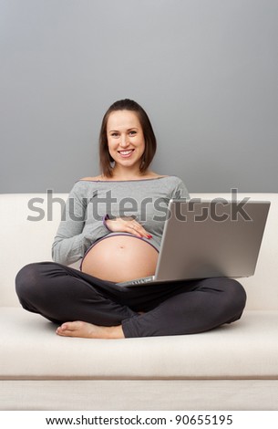 smiley pregnant woman resting on sofa with laptop
