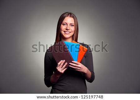 beautiful young woman holding three books. studio shot over dark background