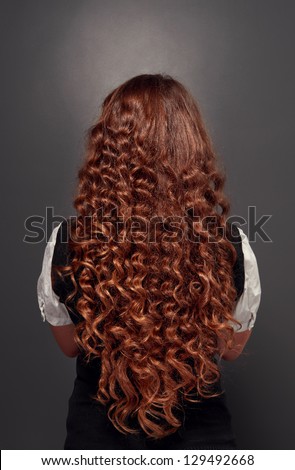 back view of beautiful natural brunette with long curly hair. studio shot over dark background