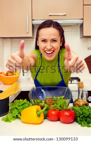 young housewife showing thumbs up and laughing at the kitchen