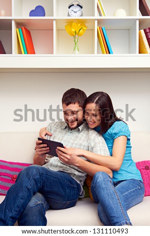 smiley young couple sitting on sofa and looking at the tablet pc