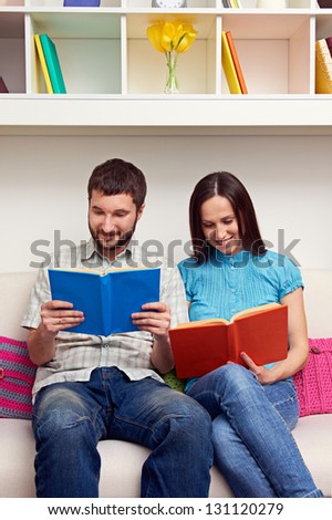 smiley couple sitting on sofa and reading books