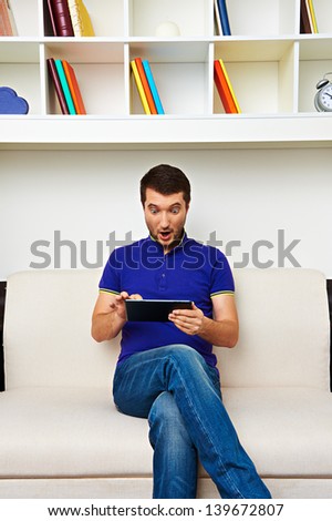 surprised man sitting on the sofa and looking at tablet pc