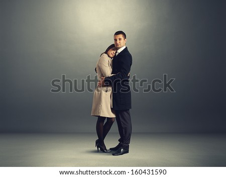 smiley woman and serious man standing over dark background