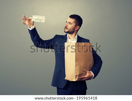 man looking at banknote and holding paper bag over dark background