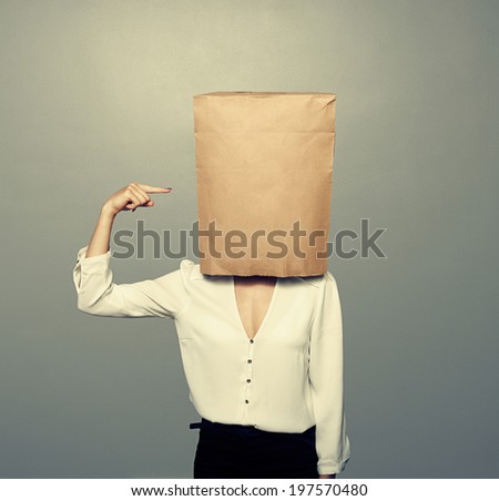 woman pointing at paper bag on the head over dark background