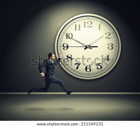 serious running businessman and big white clock in dark room