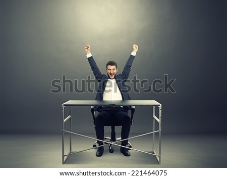 excited businessman sitting at the table, raising hands up up and laughing. photo in the dark room