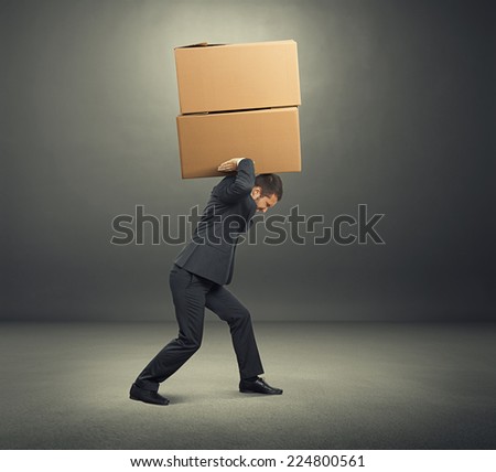 tired young businessman carrying two heavy boxes. photo in the dark room