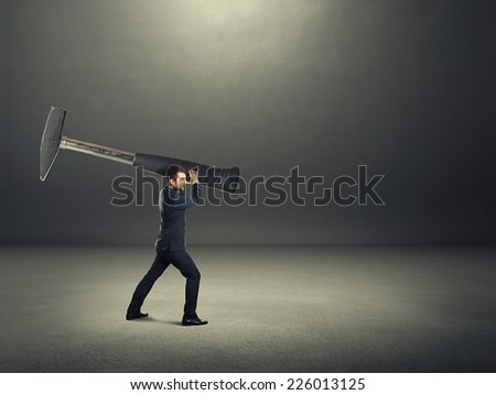 angry screaming businessman holding big hammer and hitting. photo in the dark room with empty copyspace